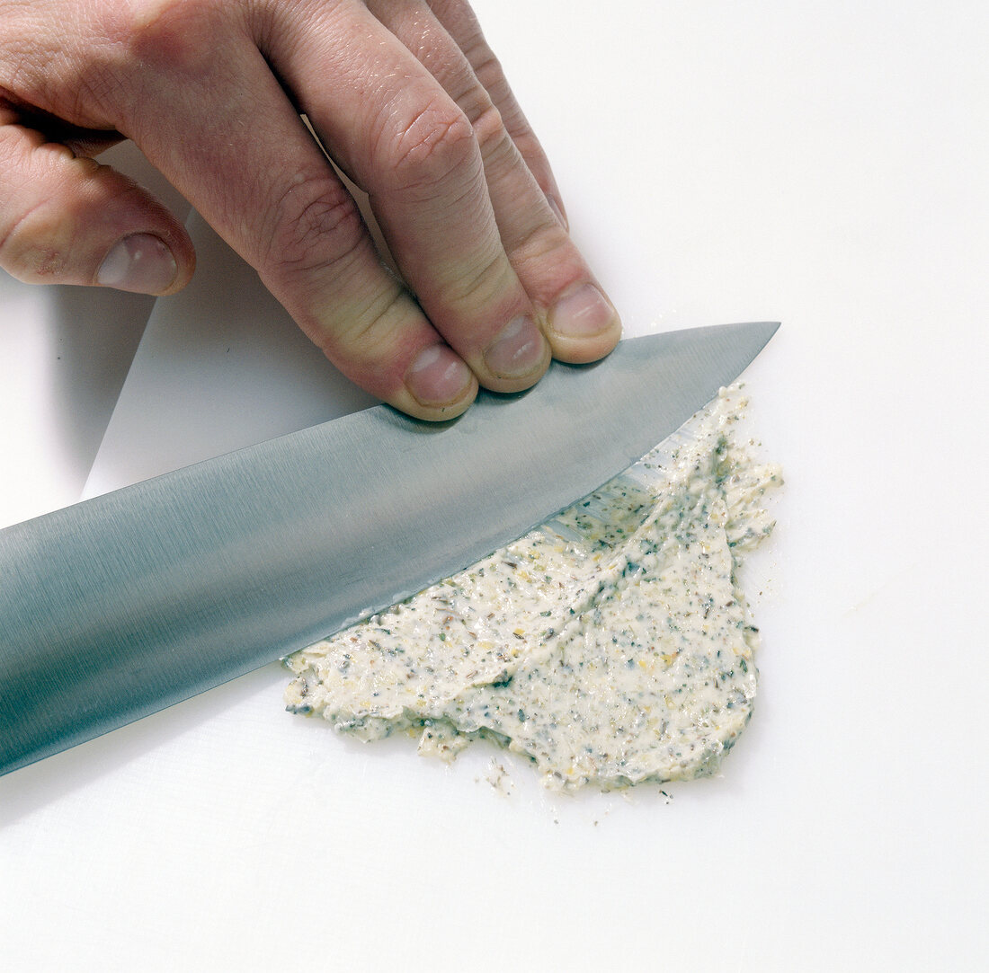 Mixture of garlic butter, dried marjoram and caraway seeds being crushed with knife