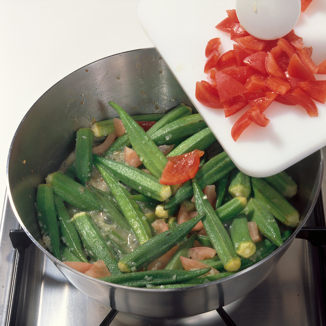 Adding diced tomatoes to okra in saucepan on stove, step 3