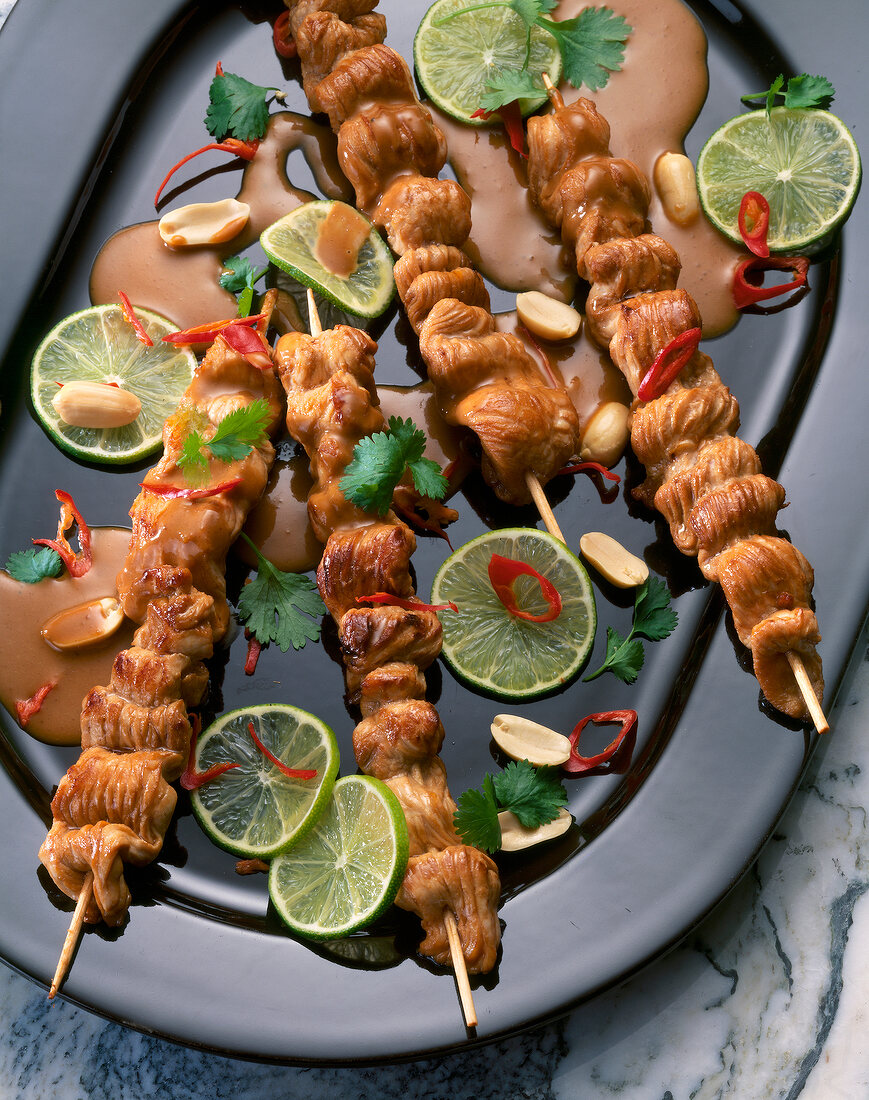 Turkey skewers with peanut sauce and lime slices on plate