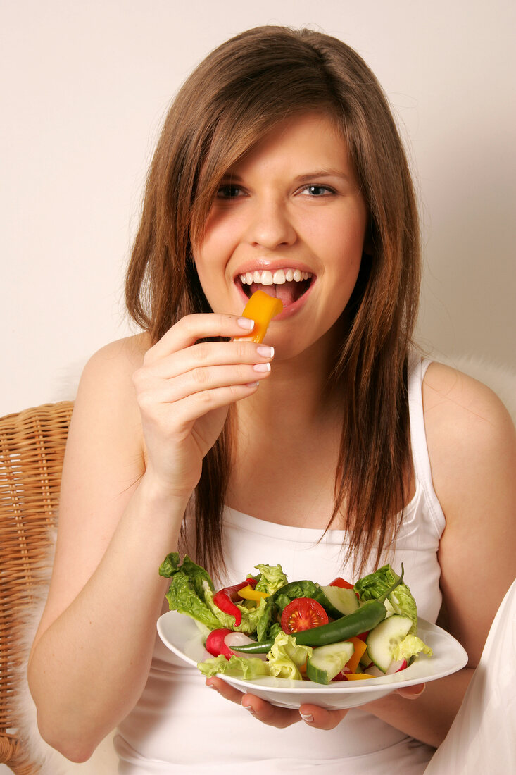 Portrait of woman with long hair eating yellow peppers with hand