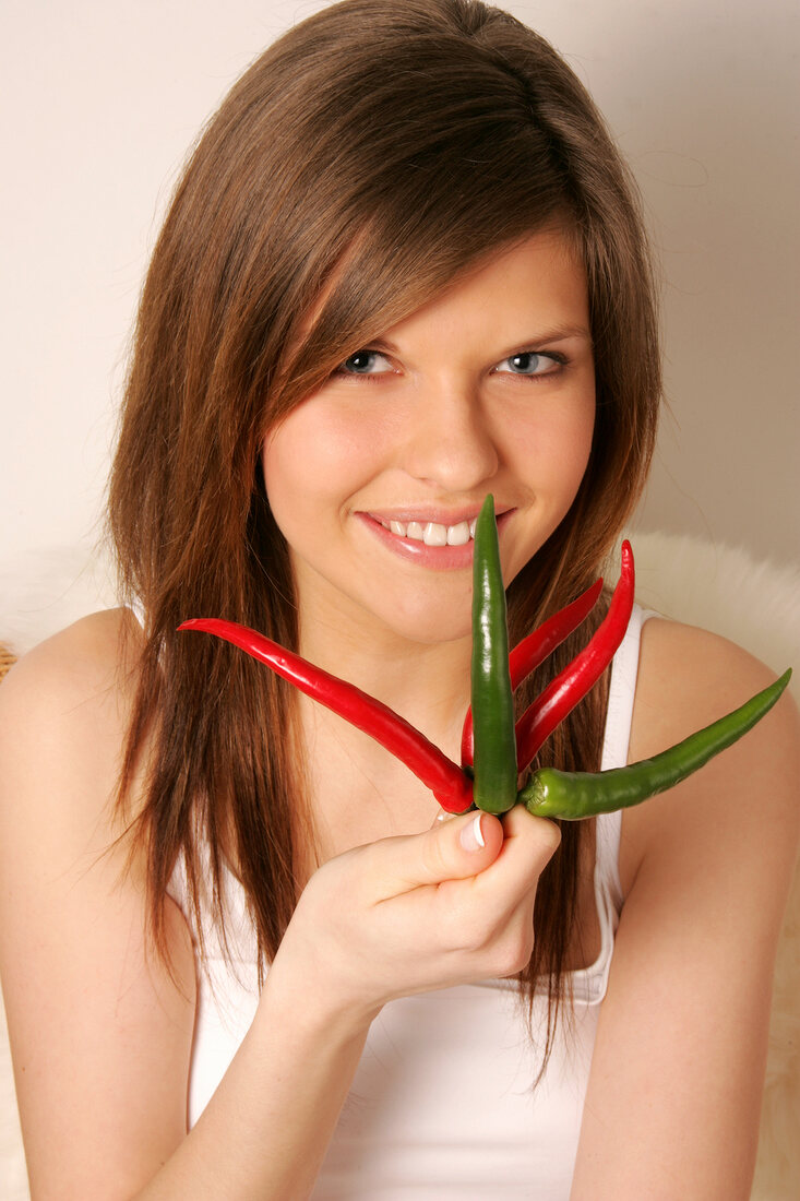 Portrait of woman with brown hair holding green and red chilies, smiling