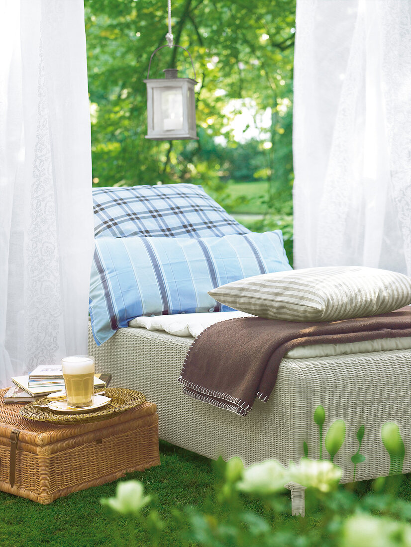 Bed with pillows and blankets next to curtains in garden