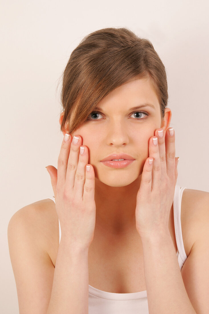 Portrait of pretty woman with brown hair massaging her face with hands