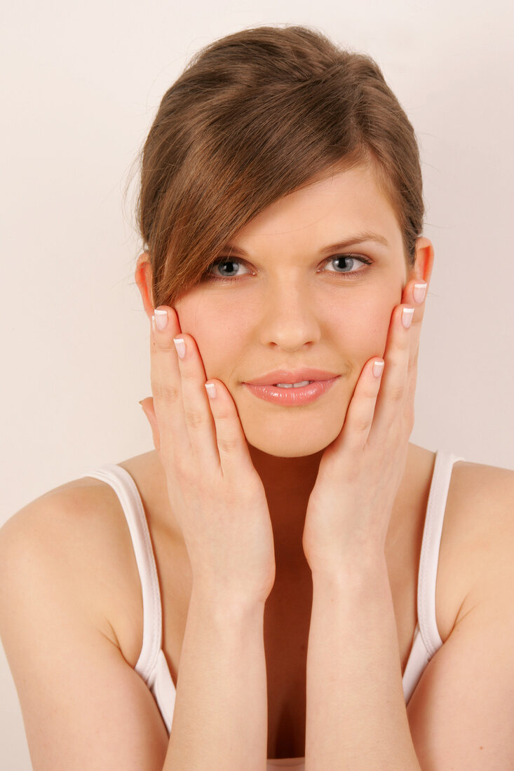 Portrait of pretty woman with brown hair massaging her face with hands