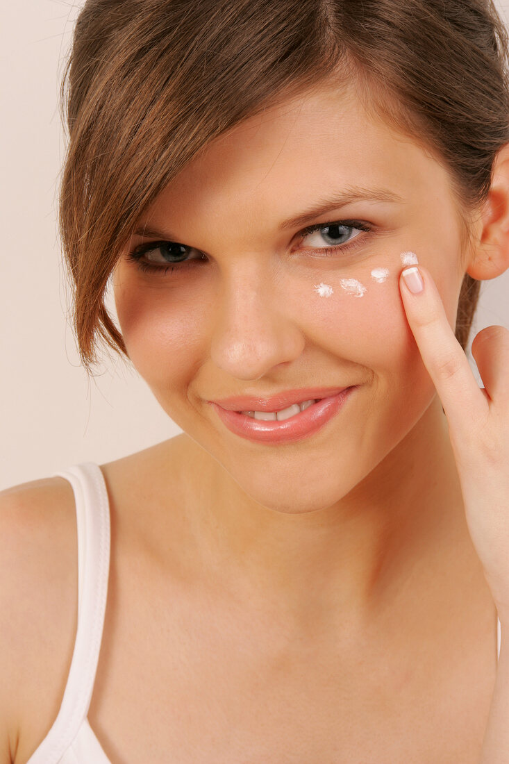 Portrait of Magdalena woman with brown hair having spots of cream under her eye, smiling