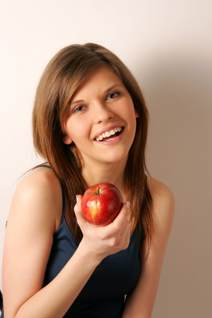 Woman with brown hair holding an apple, smiling