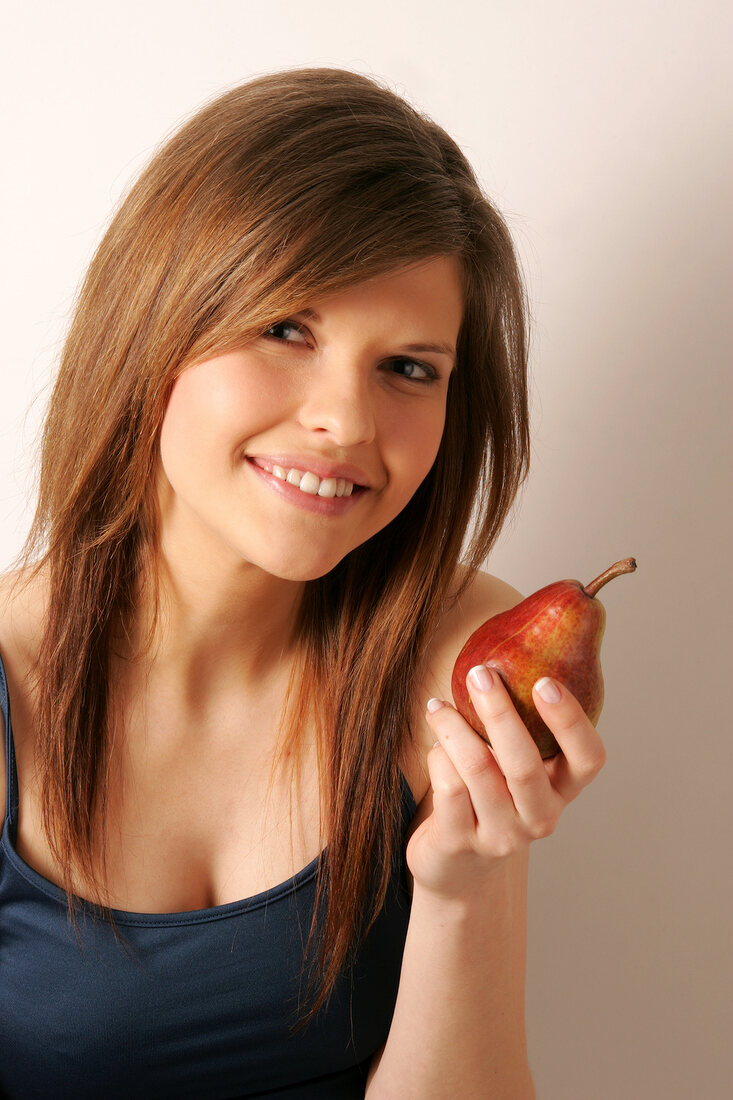 Portrait of woman with brown hair holding red pear, smiling