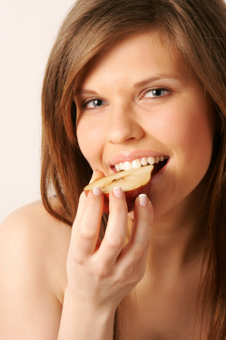 Close-up of woman with brown hair eating half red pear