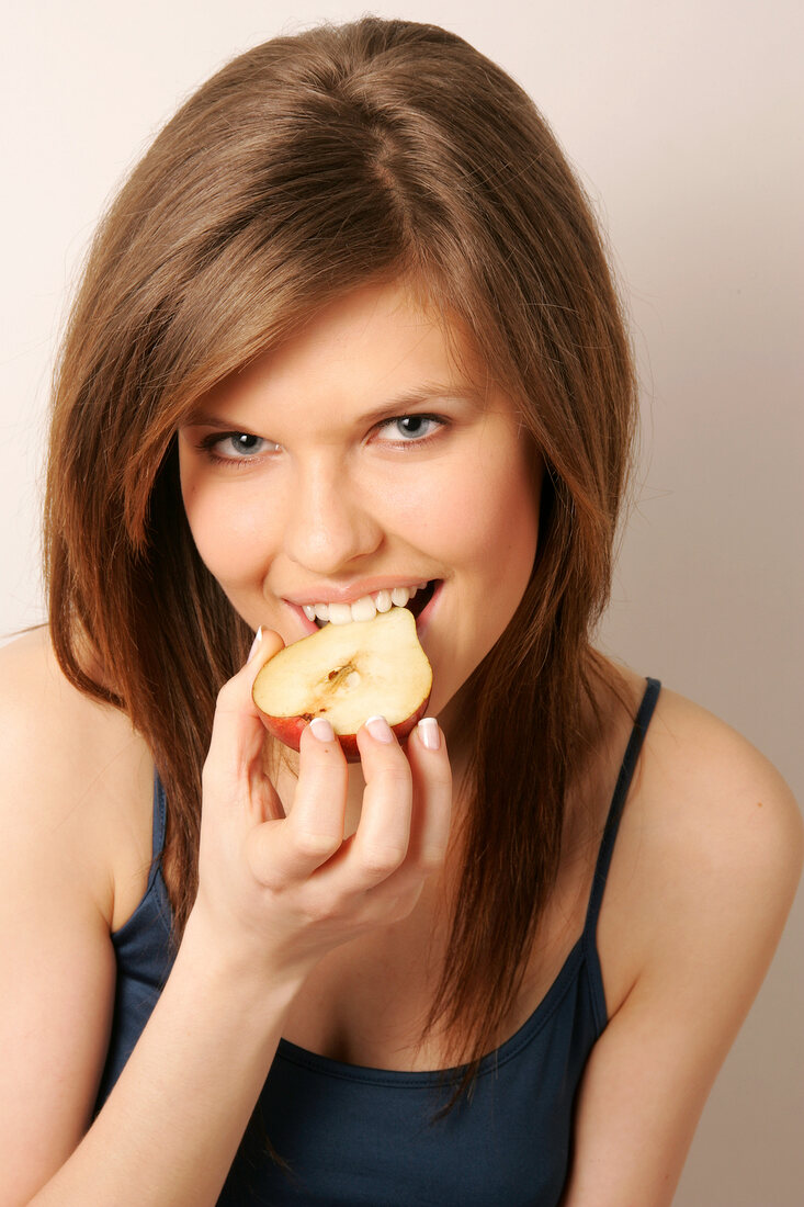 Frau mit langen Haaren isst Birne mit der Hand