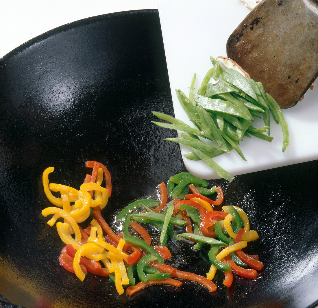 Adding vegetables to wok with slices of colourful bell peppers, step 2