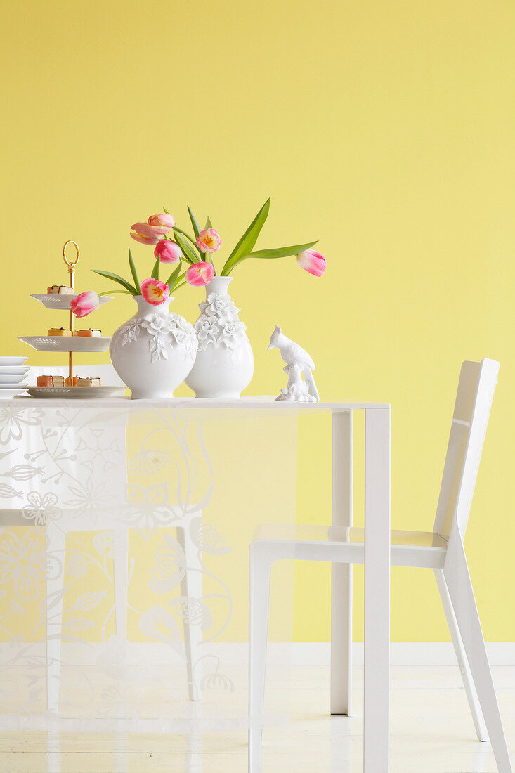 White dining table with two vases of tulips and confectionery against yellow wall