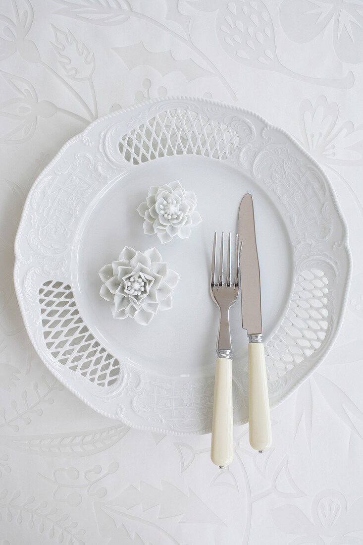 Porcelain plate with two decorative flowers and cutlery, overhead view