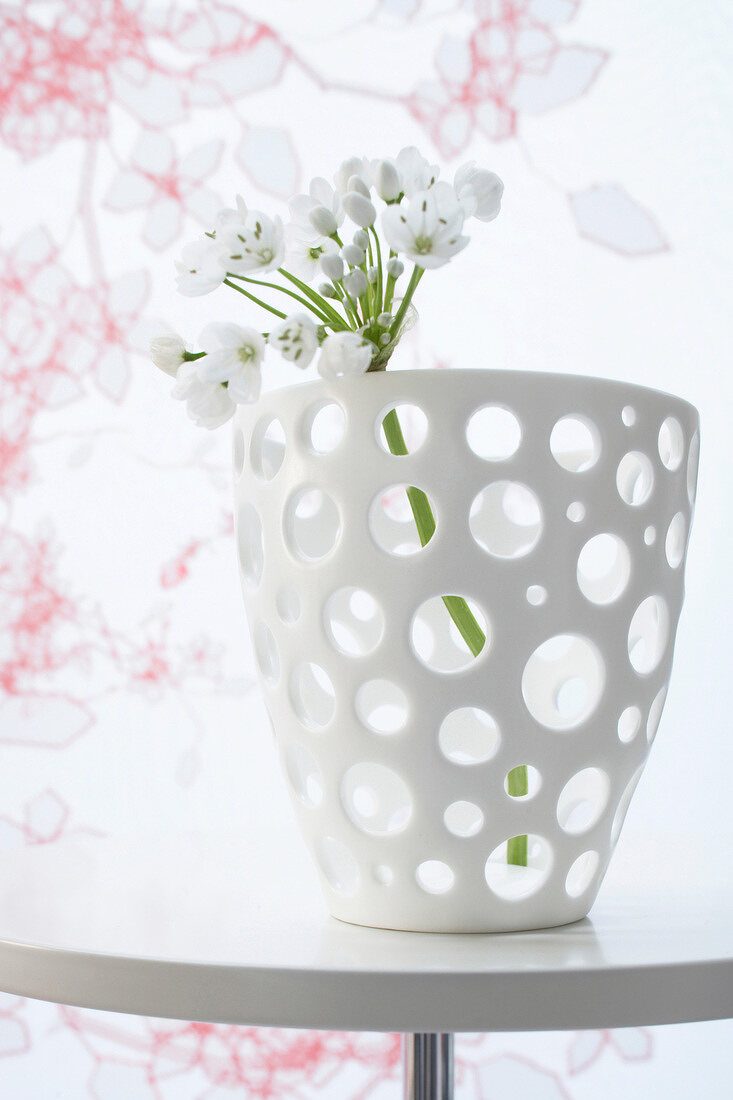 Close-up of white dot bowl with flower in front of wallpaper with tendrils