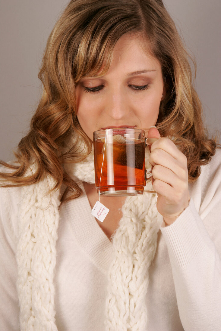 Woman with long hair wearing white sweater holding tea cup, smiling