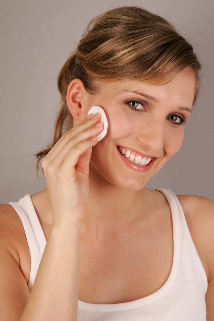 Portrait of pretty blonde woman cleansing her face with cleansing pad, smiling