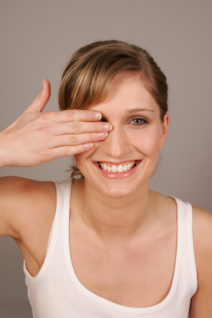 Gray eyed Charlotte woman with blonde hair covering one eye with her hand, smiling