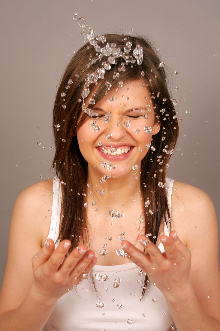 Close-up of pretty woman with brown hair cleaning her face with water, smiling