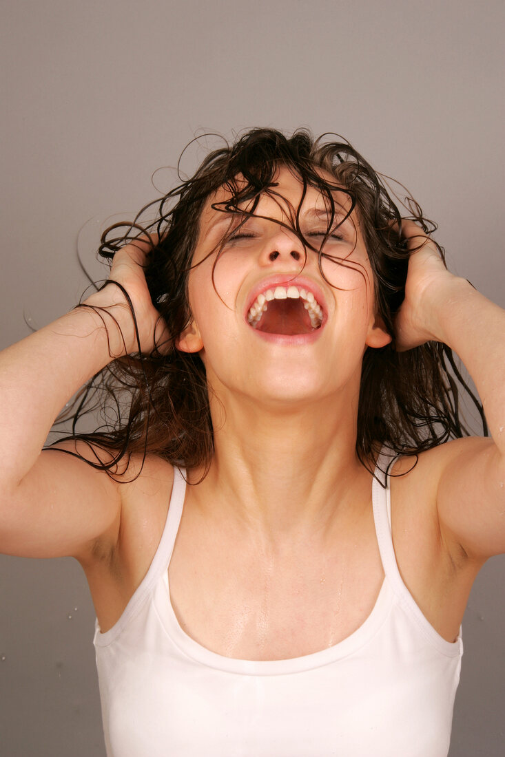 Pretty woman with wet hair wearing white top laughing with hand in hair, eyes closed