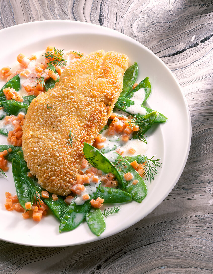 Close-up of sesame breaded fillet fish with sugar peas and carrots on plate