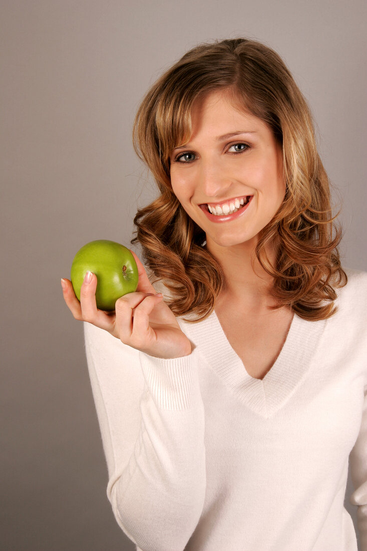 Portrait of young woman holding green apple and smiling