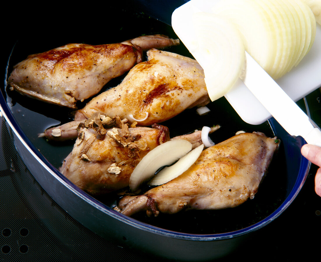 Onion's being added to rabbit's meat with mushrooms in cooking pan