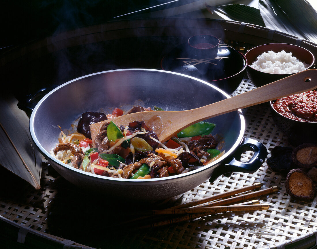 Preparation of Asian dish in casserole with wooden spoon