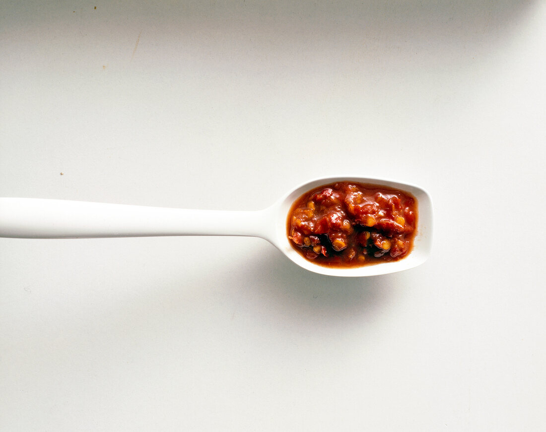 Red spice paste on a plastic spoon on white background