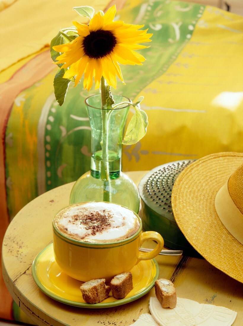 Yellow cup of coffee with sunflower vase on wooden table