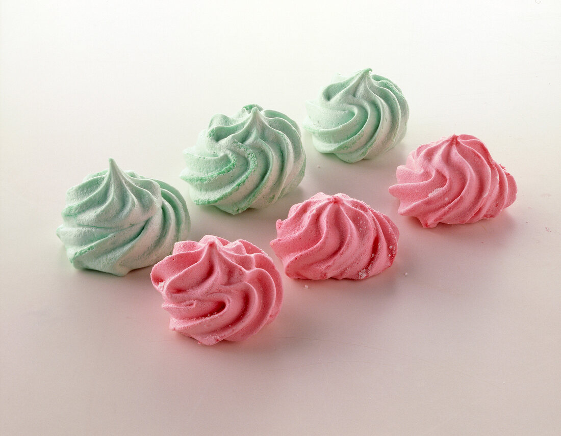 Three meringues in pink and pale green colour on white surface
