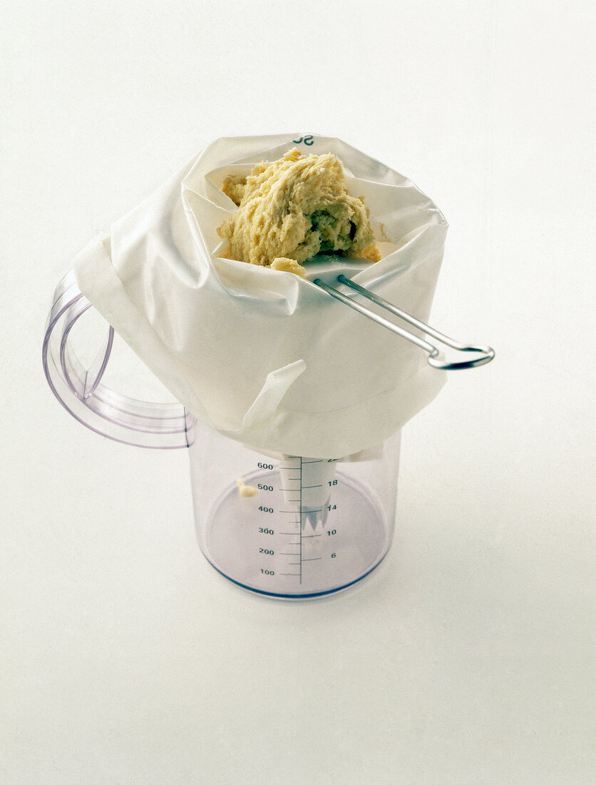 Measuring cup with pastry bag kept on white background