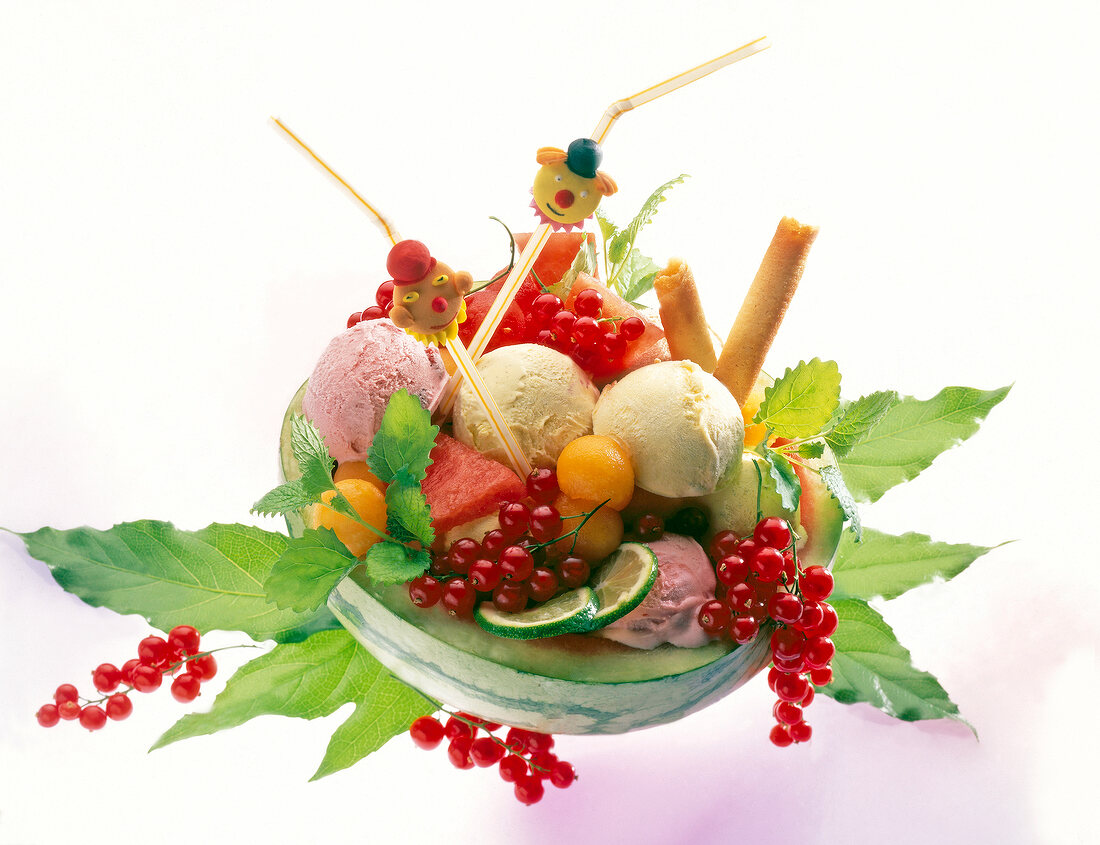 Watermelon with ice cream scoops, red currants and lime against white background