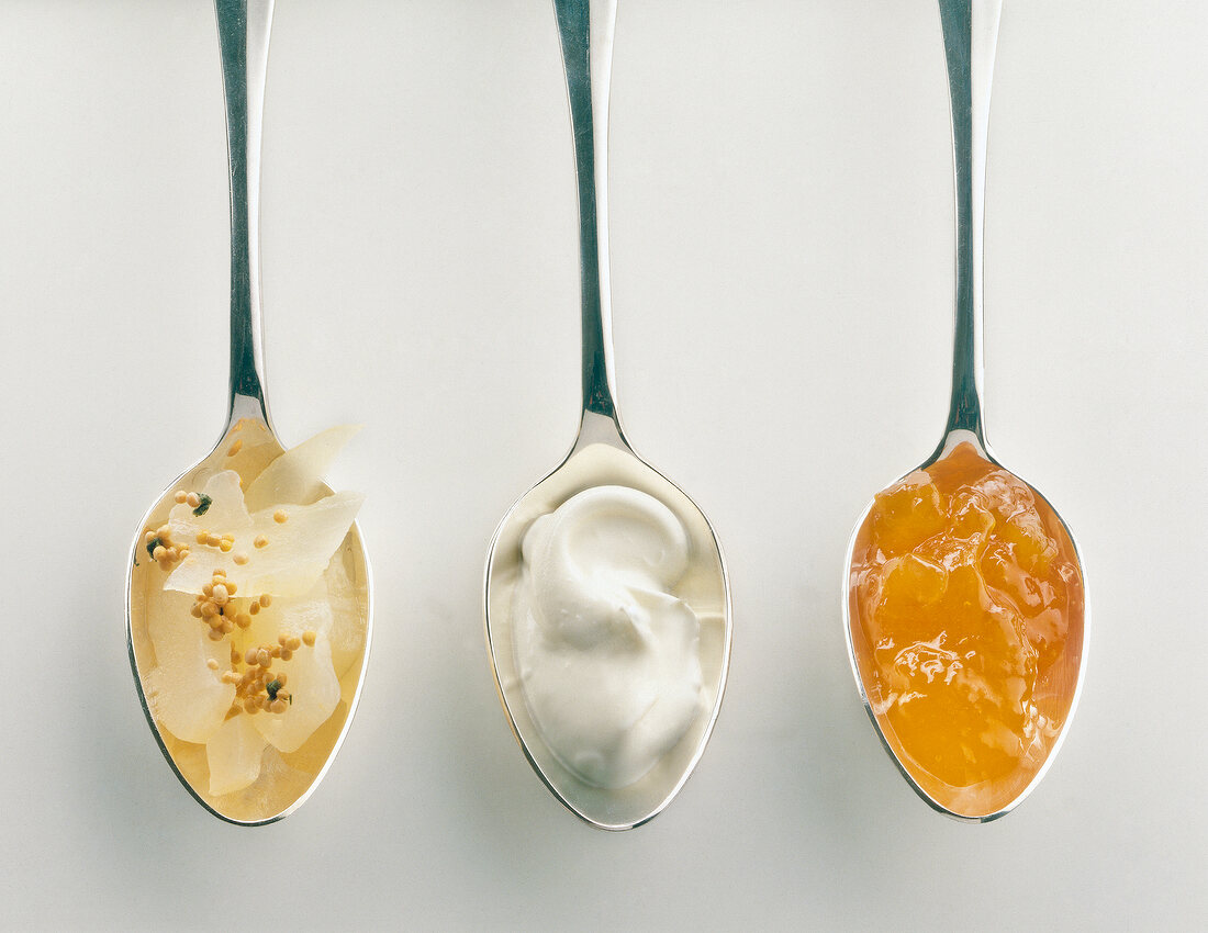 Three spoons with fruit chutney, fresh cream and jam on white background