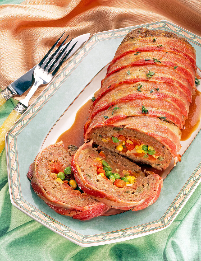 Sliced meatloaf stuffed with capers, vegetables and bacon on serving tray
