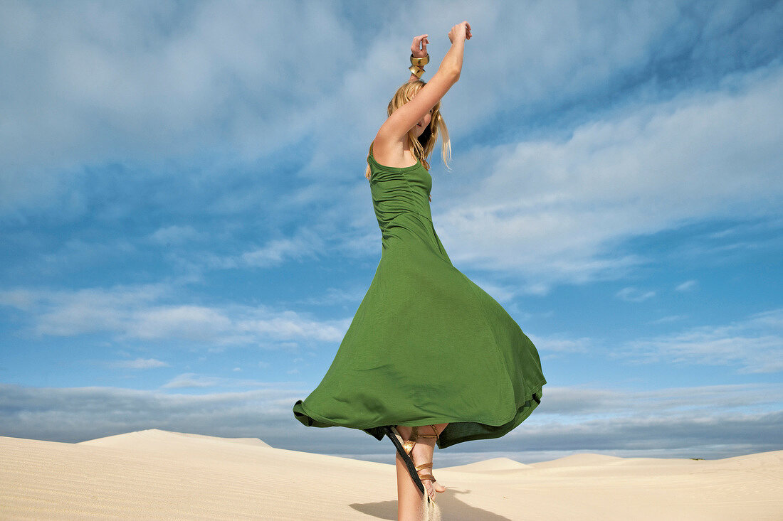 blonde Frau in grünem Kleid tanzt in der Wüste