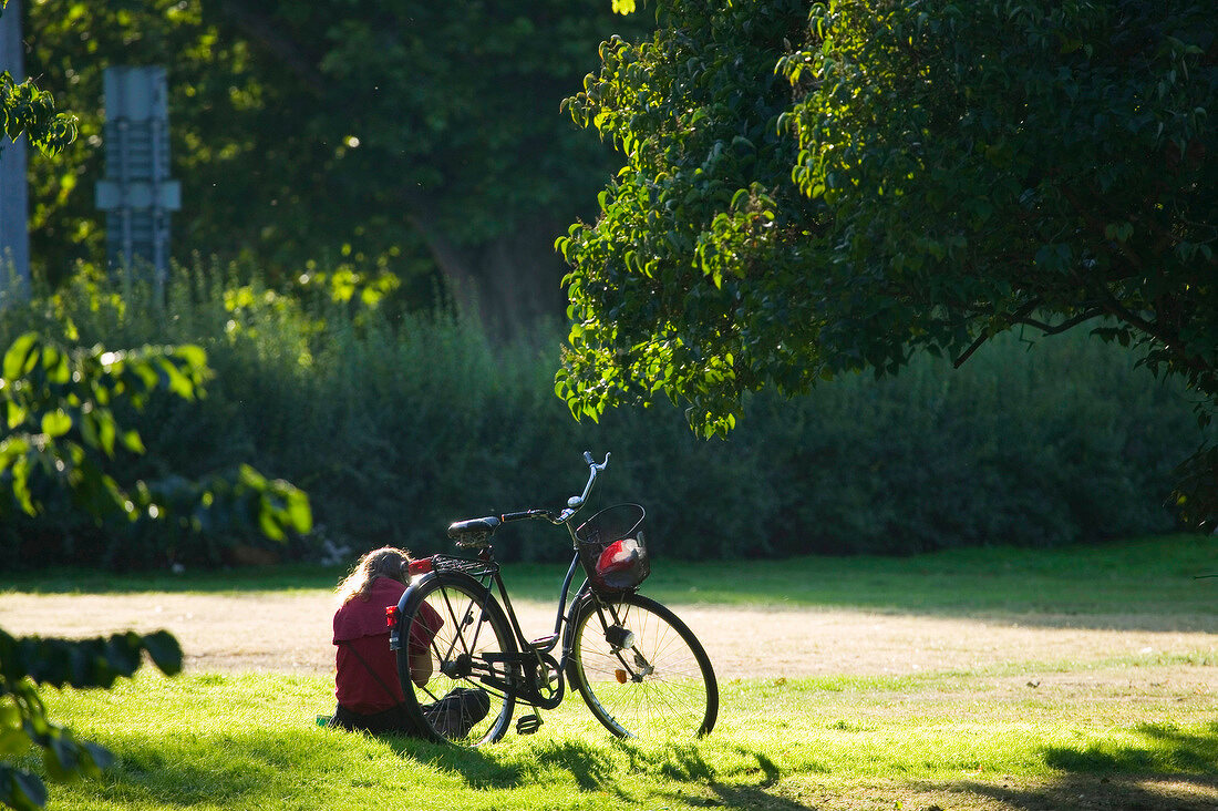 Frau sitzt  neben ihrem Fahrrad im Kungsparken in Malmö, Schweden.