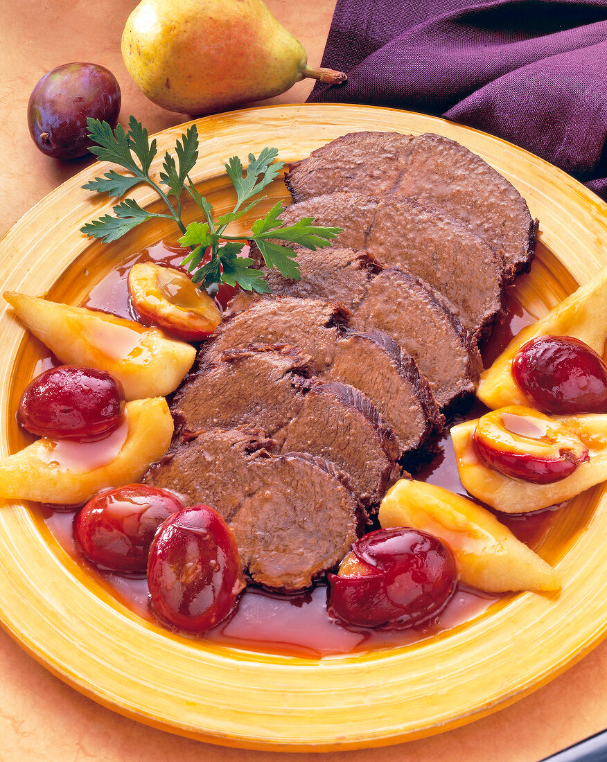 Sauerbraten in Scheiben mit Birnen und Pflaumen auf Teller