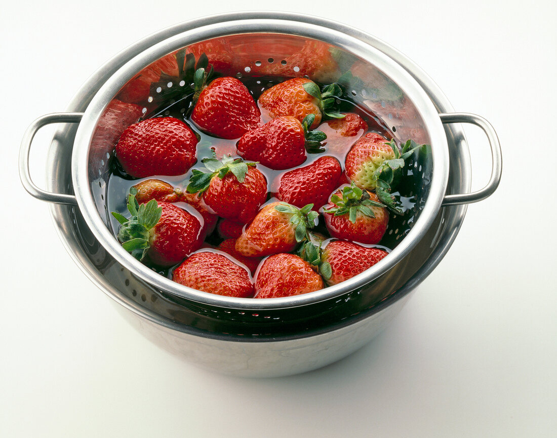 Strawberries and pivot berries being washed in water on white background