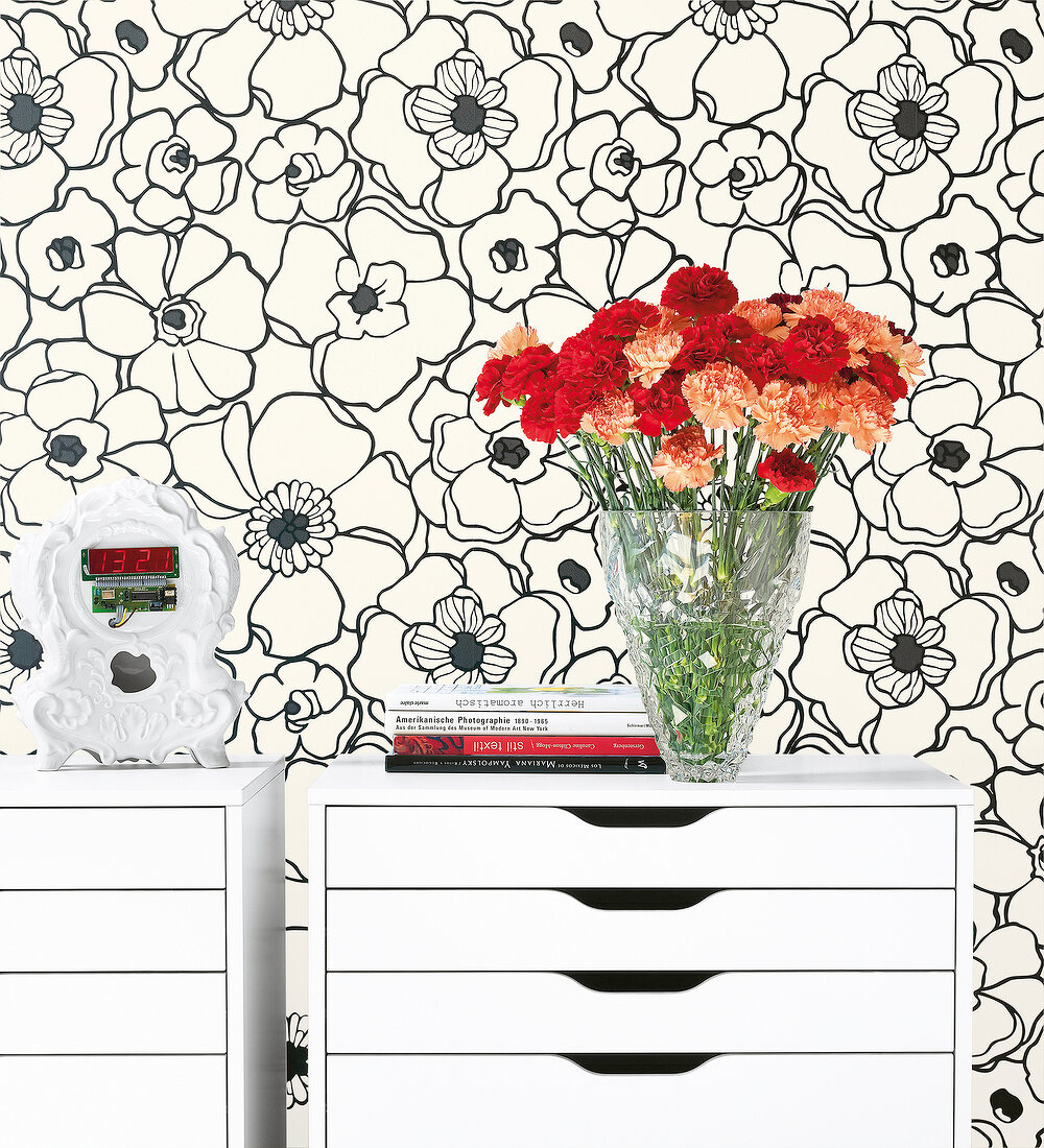 Close-up of flower vase on chest of drawers against floral printed wall