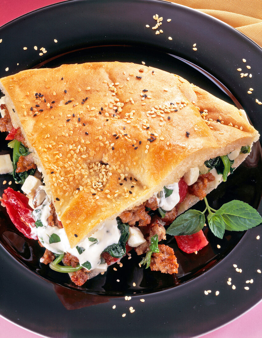 Close-up of flatbread filled with colourful hack, spinach, mozzarella cheese and yoghurt