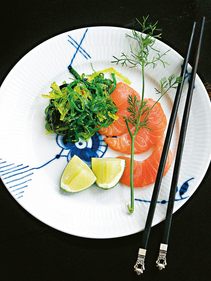 Lachs mit Algensalat, Limetten und Dill auf Teller, Essstäbchen