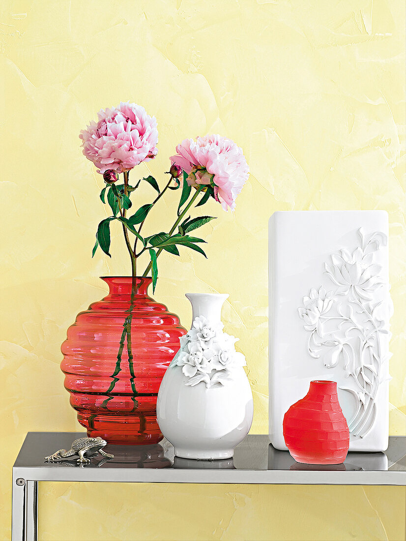 Versch. Vasen in Rot und Weiß, rosa Pfingstrosen, Wand gelb