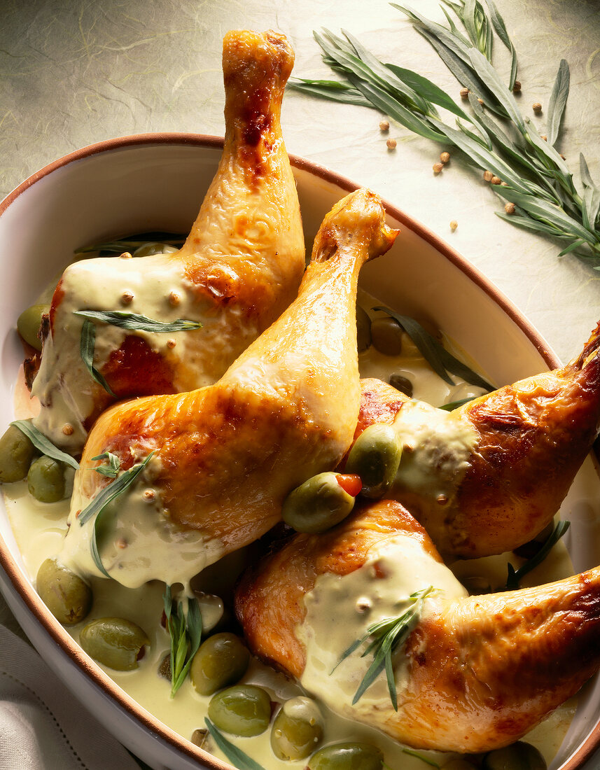 Close-up of chicken legs with olives and sauce in bowl