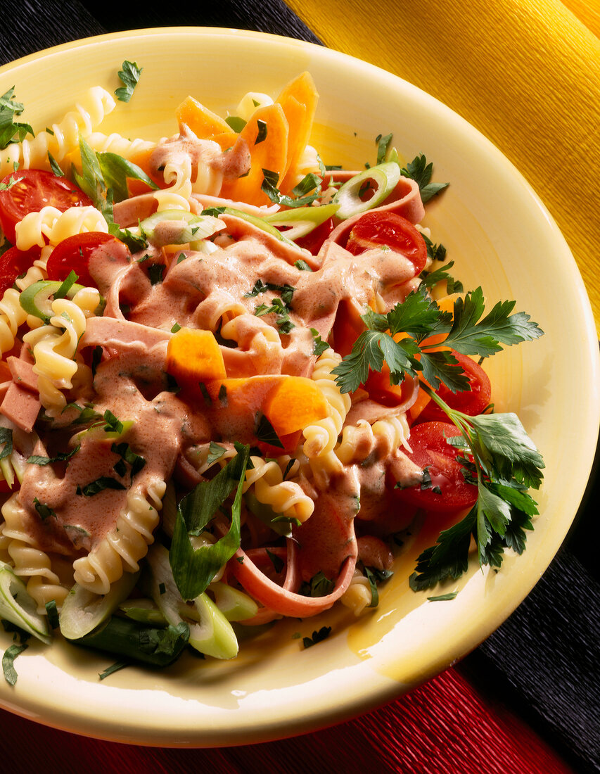 German sausage noodle salad with tomato and parsley in bowl