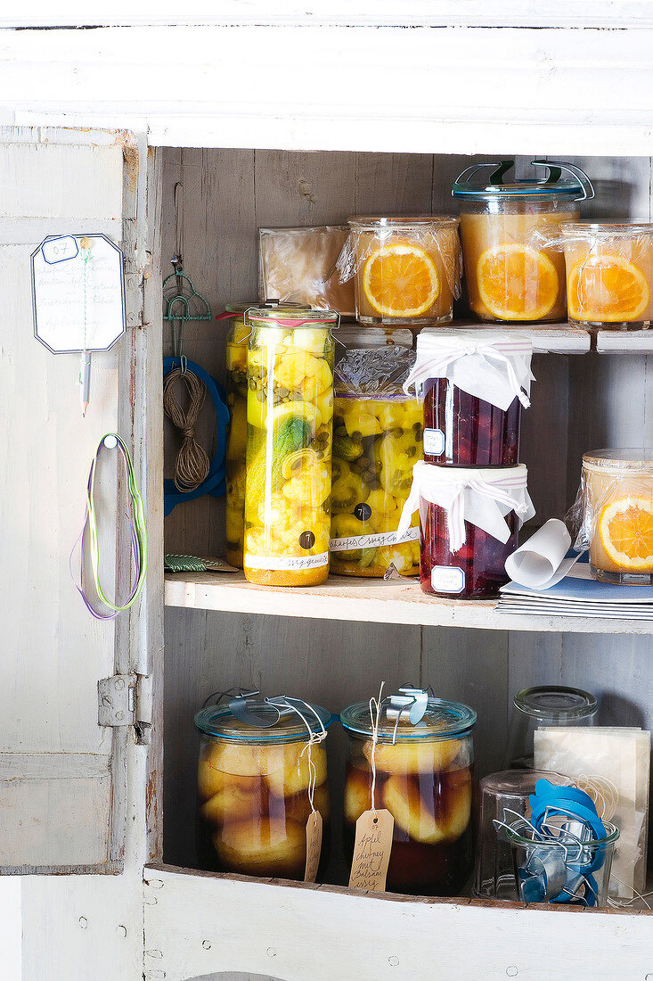 Glass jars of mustard, pickles, apple balsamic chutney and plum relish in shelves