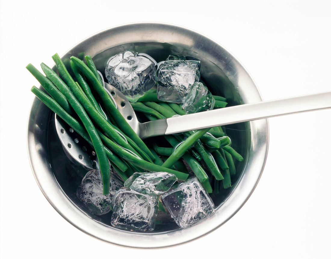 Green beans in bowl of water with ice cubes