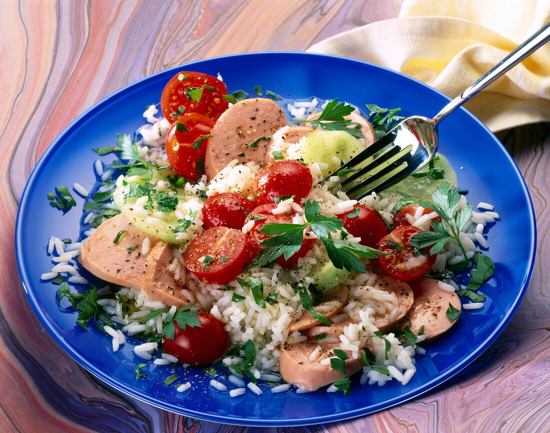 Rice salad with sausage, tomatoes and herbs on blue plate