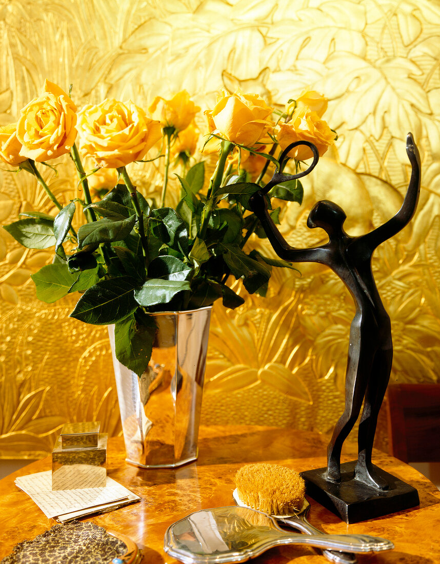 Close-up of yellow roses in vase with human figurine on table
