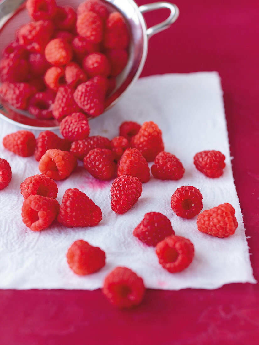 Close-up of raspberries in sieve and on kitchen paper