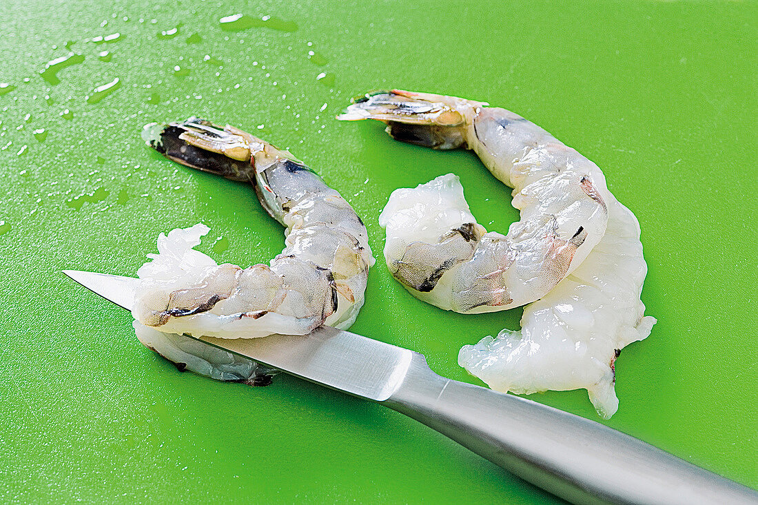 Close-up of halved shrimps with knife on green background