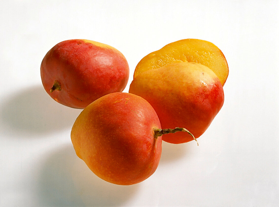 Whole and halved yellow and red mangoes on white background